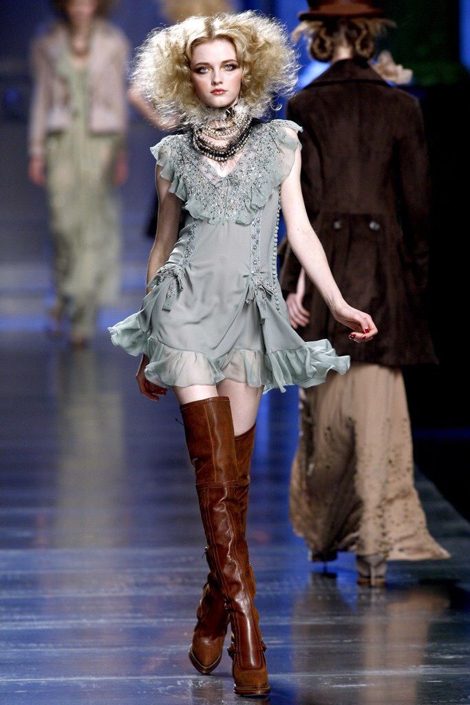 model habiller avec une robe vert pale avec plein de bijoux accrocher au cou et des bottes qui lui arrive au dessus des genoux