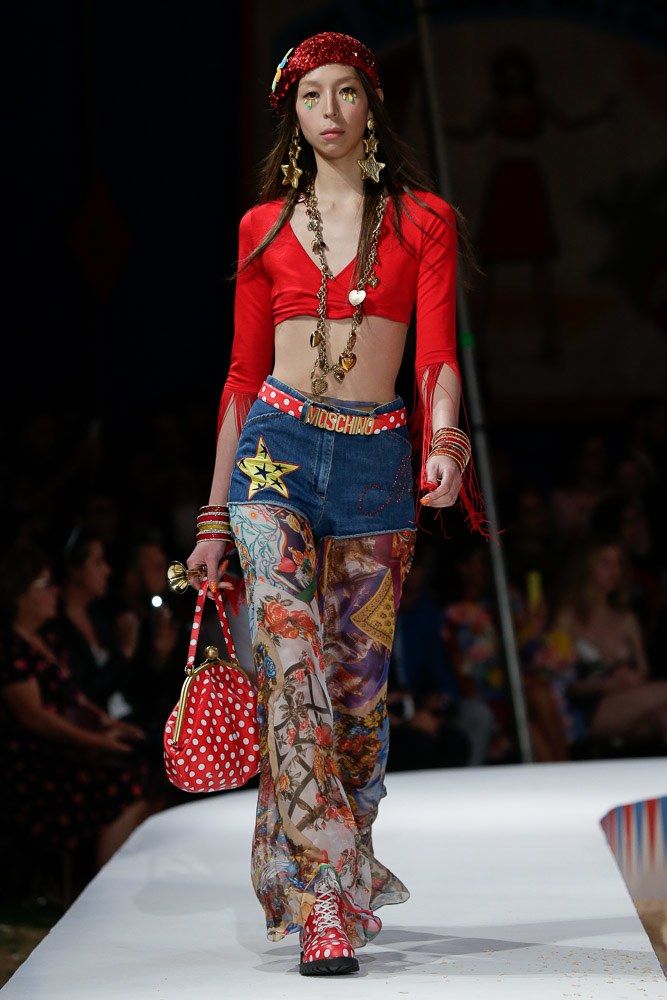 model qui porte des pantalon très colorer avec un chandail rouge fluo, elle a des accessoires doré un un sac picoter
